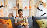 A woman sits on a couch watching scary TV shows.