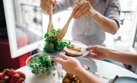 Someone serves a salad onto another person's plate.