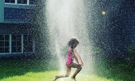 A girl jumps through a sprinkler in a Woodbury backyard.