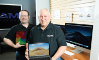 Team Technology shows off a Macbook with an iMac in the background.