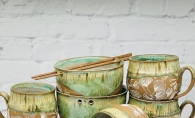 Mugs and bowls with green glaze and ginkgo leaf patterns by Paula Clegg.