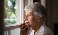An elderly woman looks out a window.