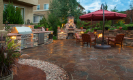 A beautiful outdoor space after a patio renovation, featuring a fireplace, grill, seating, brick floors and more.