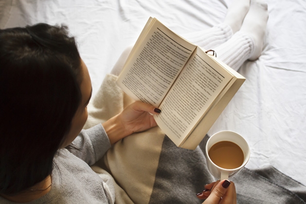 A woman reads Erik Larson's "The Strange Case of the Alchemist's Daughter" while drinking a cup of coffee.