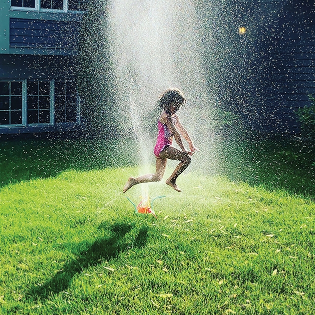 A girl jumps through a sprinkler in a Woodbury backyard.