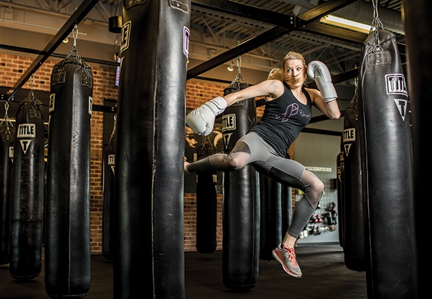 TITLE Boxing Club Woodbury Sarah Krotz, a coach at TITLE Boxing Club Woodbury, kicks a punching bag.