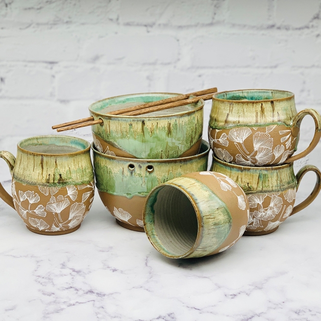 Mugs and bowls with green glaze and ginkgo leaf patterns by Paula Clegg.