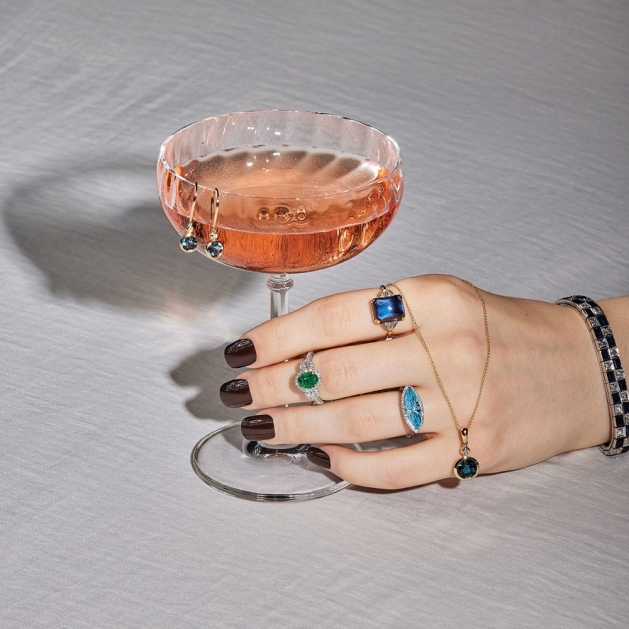 Hand holding a cocktail class bejeweled with rings, necklaces and bracelets.