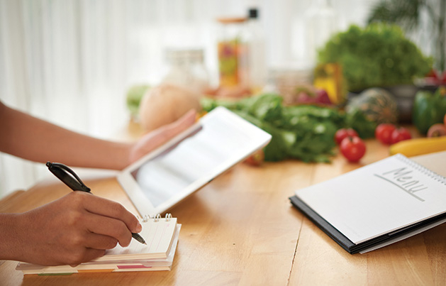 A person plans a healthy menu using a tablet and a notebook.