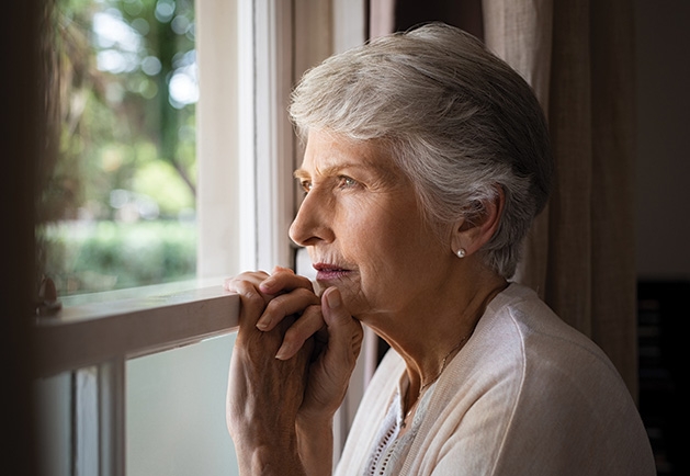 An elderly woman looks out a window.