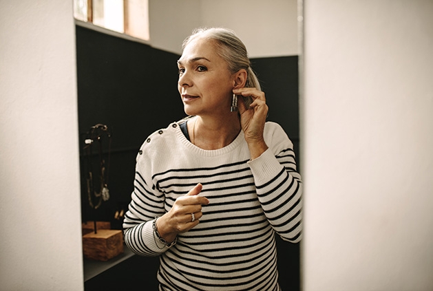 A woman tries on earrings in a mirror.