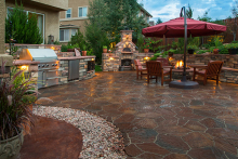 A beautiful outdoor space after a patio renovation, featuring a fireplace, grill, seating, brick floors and more.