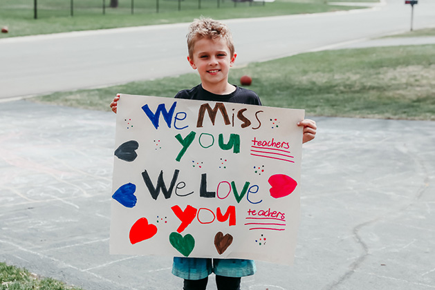 A Red Rock Elementary student holds a sign reading "We Miss You Teachers, We Love You Teachers