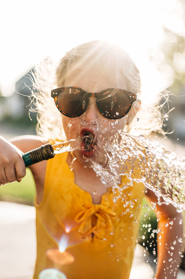 A girl drinks from a hose on a sunny day.