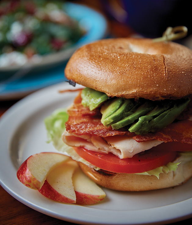 A bagel sandwich with turkey, avocado and bacon, and some apple slices, from Lake Elmo Coffee